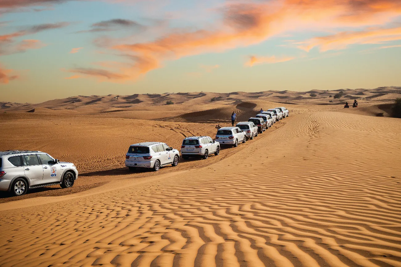A convoy of safari vehicles crossing the dunes