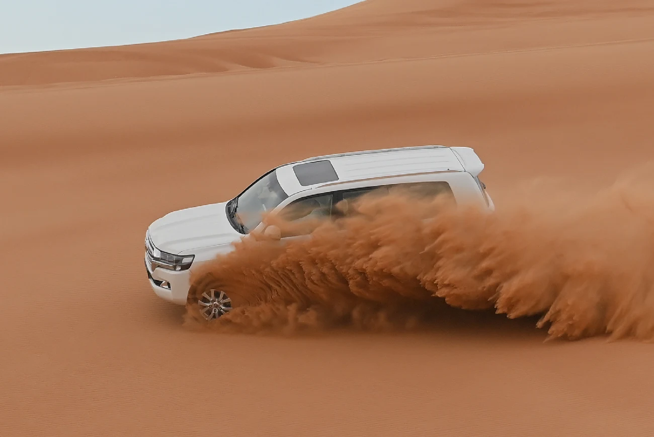 White four-wheel-drive vehicle turning through a dune and throwing up sand