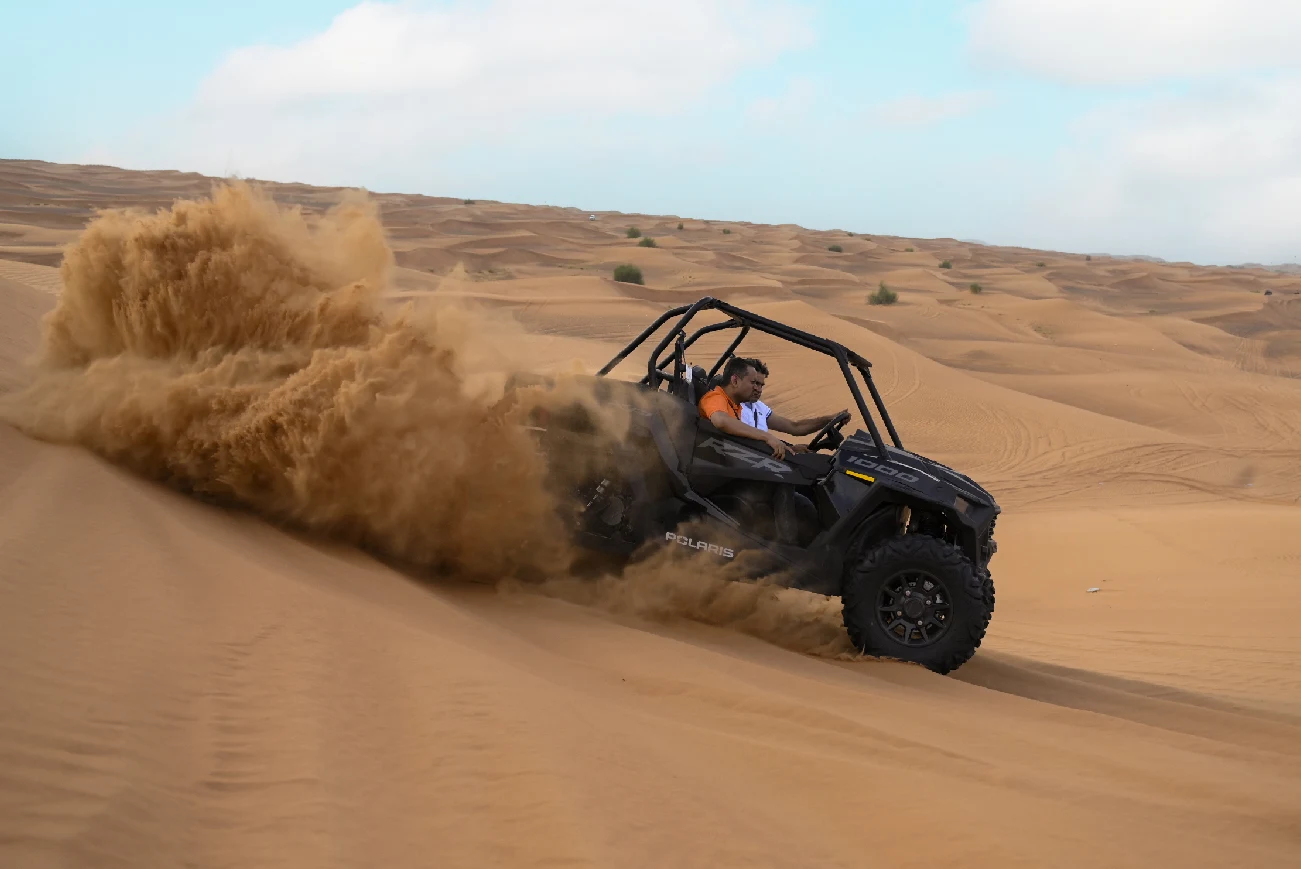Two people riding in a dune buggy as sand sprays behind it